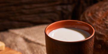 A rustic ceramic cup filled with milk on a textured surface.
