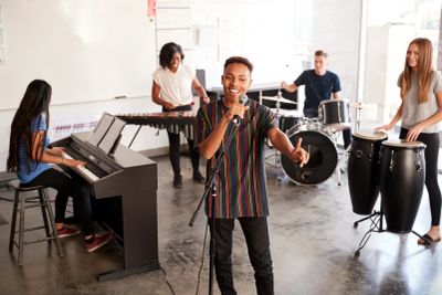 A young man sings with a band playing various instruments in a spacious room.