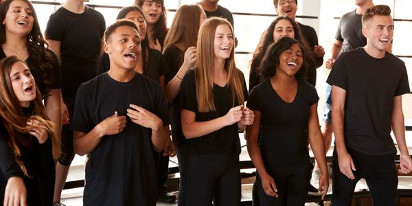 A diverse group of young people singing joyfully in a choir rehearsal.