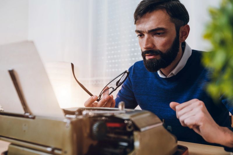 Hipster writer reading what he wrote on typewriter.