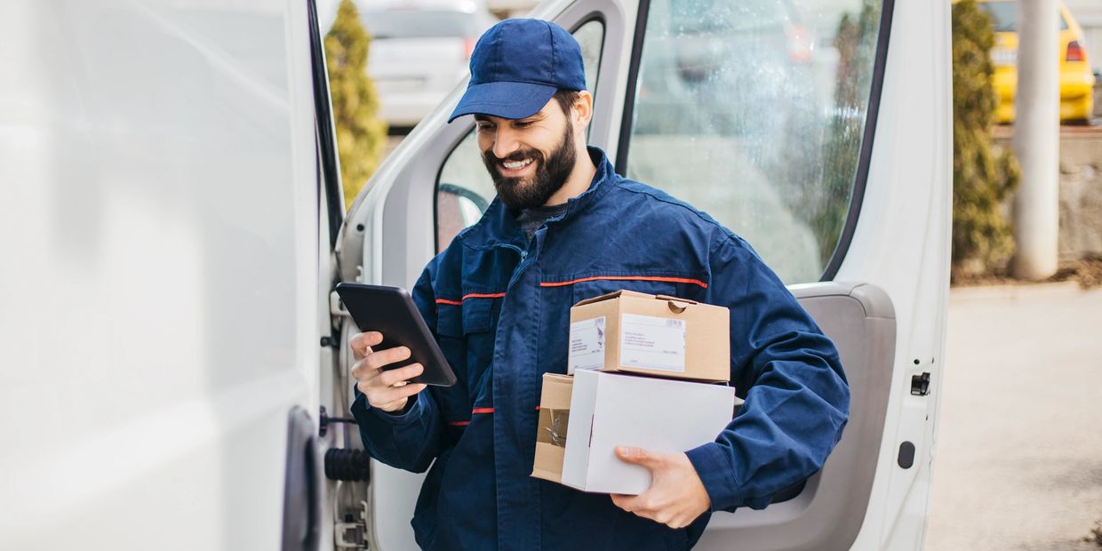 Delivery man holding packages and checking a digital device by a van door.