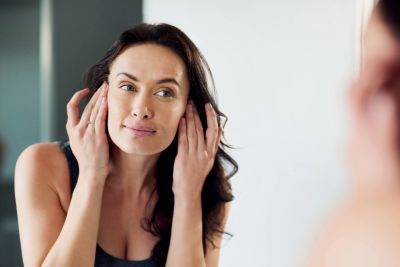 Woman examining her face in the mirror with a thoughtful expression.