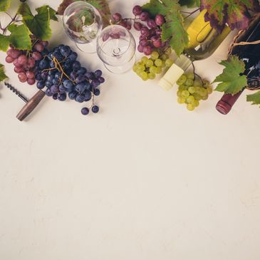 Assorted grapes, wine bottle, glasses, and corkscrew on a white surface.