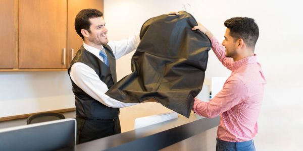 Hotel receptionist gives a garment bag to a guest.