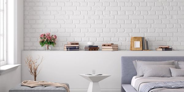 Modern bedroom with gray bed, ottoman, and white brick wall.