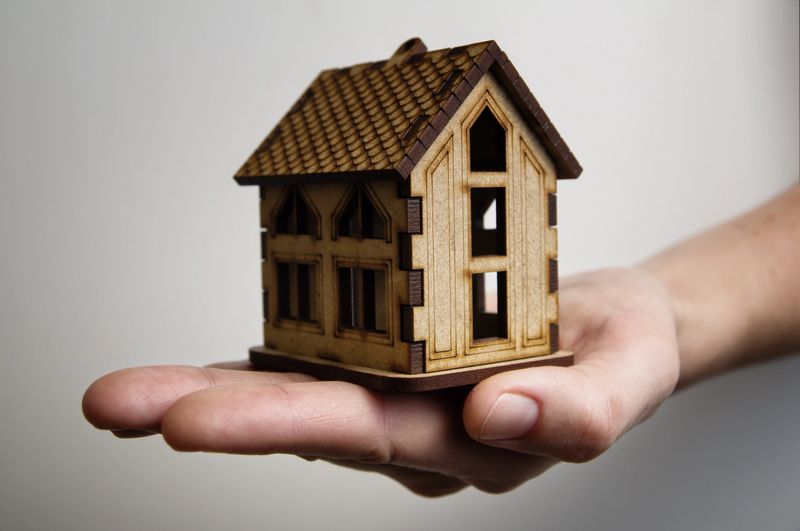 The palm with wooden model house. Concept of rent, purshase, insuranse, building real estate, eco house and other.