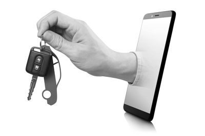 Hand holding car keys emerging from a smartphone screen.