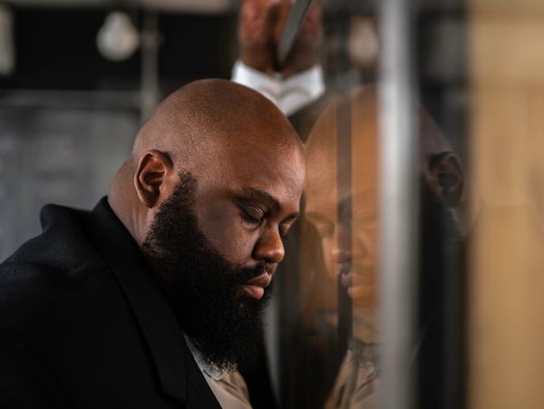 A man with eyes closed resting his head against a glass surface.