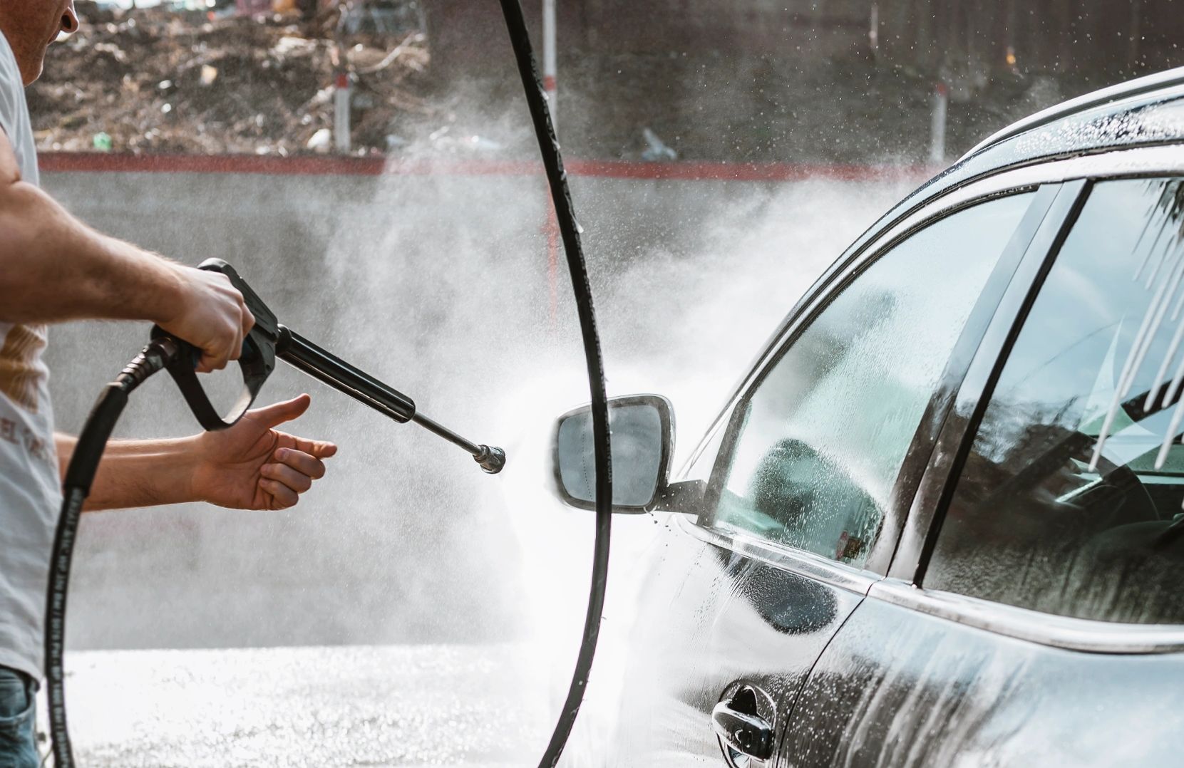 A person washing a black car with a high-pressure water hose.