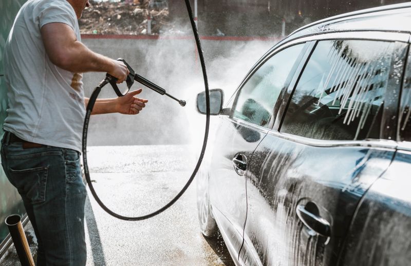 Man, wahsing his car in the stall of a car wash, using a high pressure water jet .Shot of a man washing his car under high pressure water outdoors.