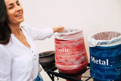A woman smiling while disposing of waste in labeled recycling bins for plastic and metal.
