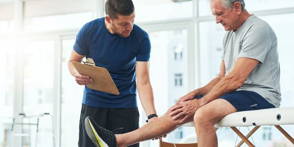 Physical therapist examining elderly man's knee during rehabilitation session.