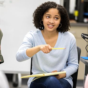 Young woman holding a pencil and notepad, engaged in discussion.