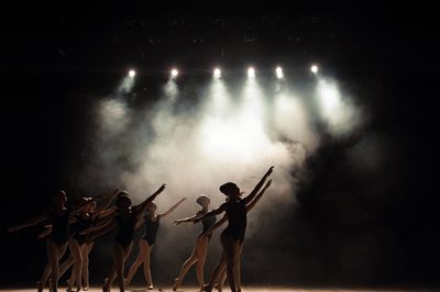 Silhouetted ballet dancers perform under bright stage lights and smoky atmosphere.