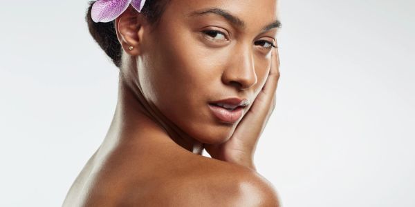 Close-up of a woman with a flower in her hair, touching her face gently.