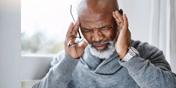Elderly man holding his head, appearing stressed or in pain.