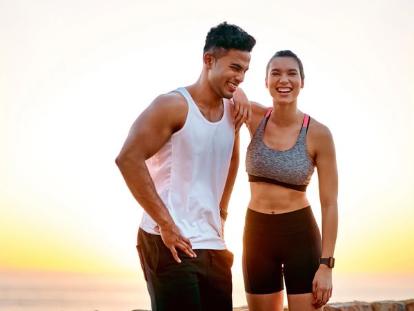 Fit young couple in workout attire smiling at sunset outdoors.