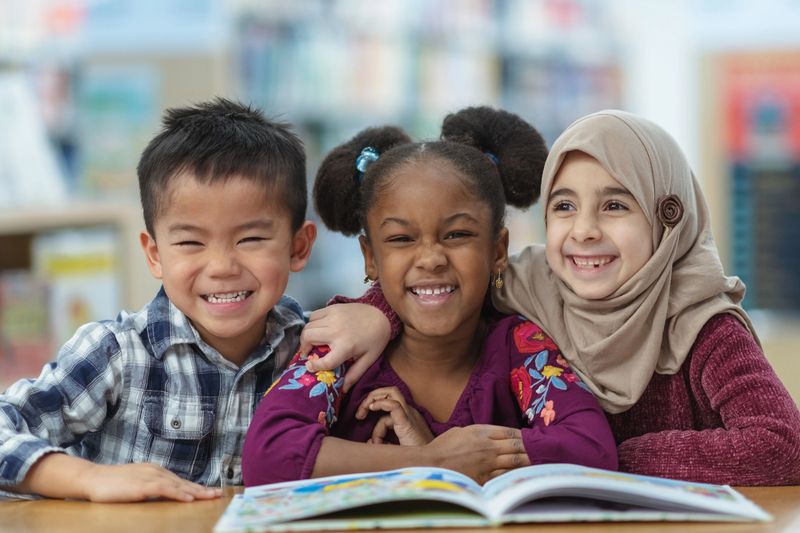 Three diverse children smiling together while reading a book.