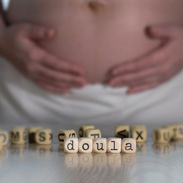 Wooden blocks spelling 'doula' with a pregnant belly in the background.
