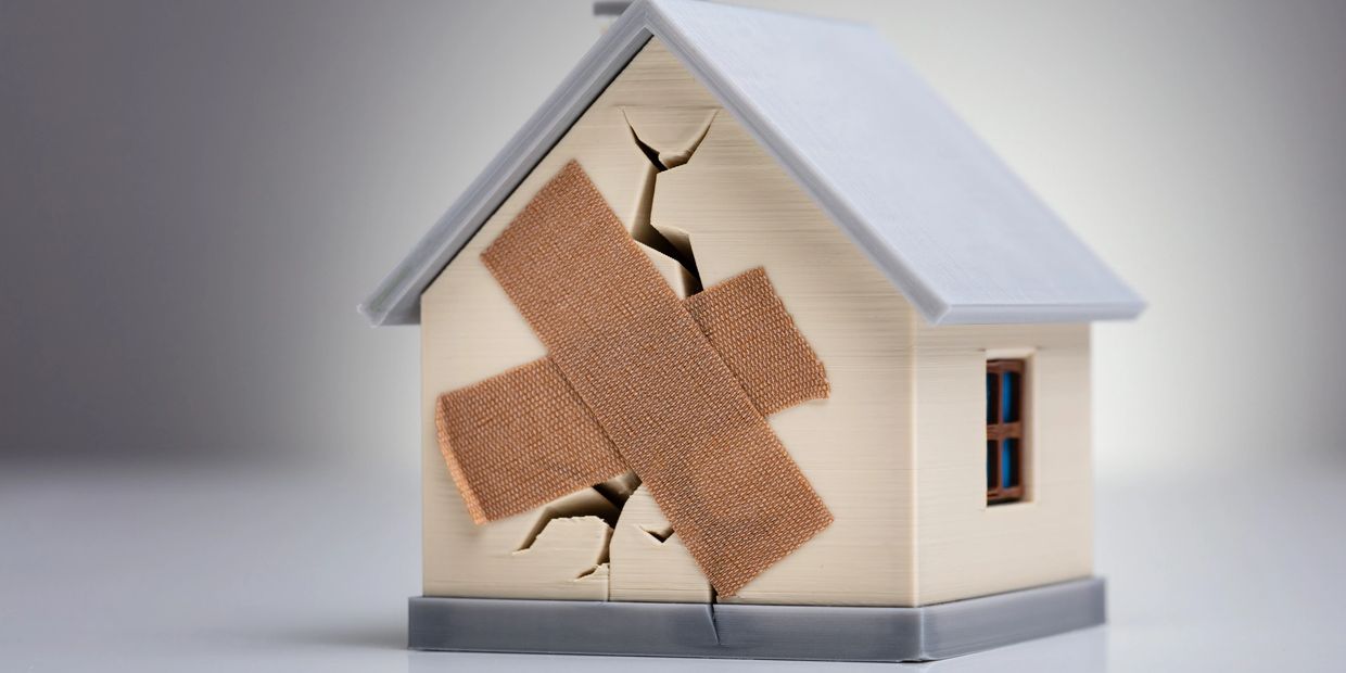 Model house with cracks patched by adhesive bandages, symbolizing repair.