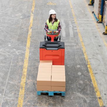 Warehouse worker operating pallet jack moving boxes on a pallet.