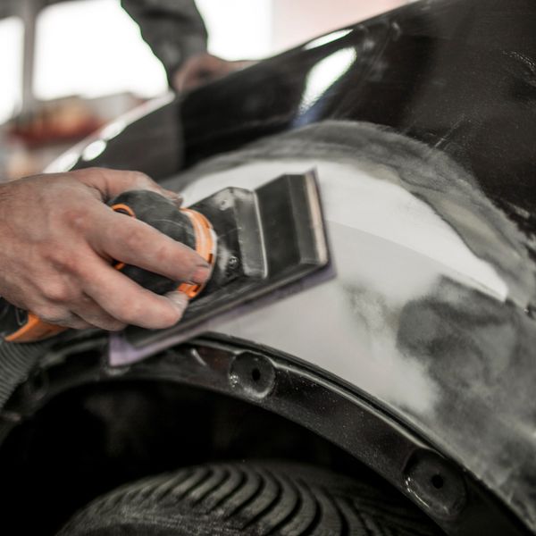 Hand sanding a car's body panel near the wheel.