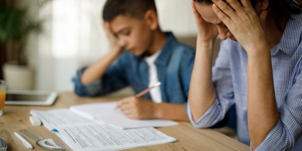 A stressed adult and child working on homework at a table.