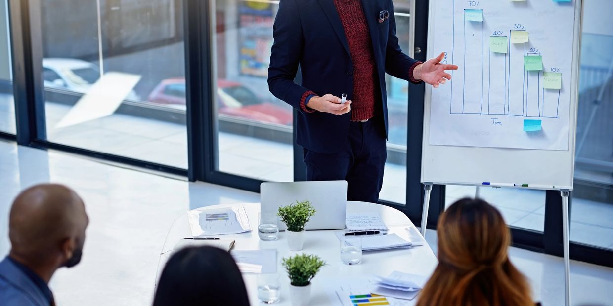A professional giving a presentation with a chart on a whiteboard to colleagues.