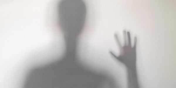 Silhouette of a person behind frosted glass, hand raised.
