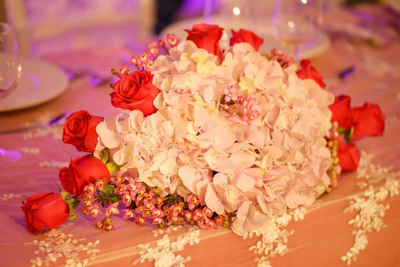 Horizontal perspective of classy floral arrangement in a pastel oval bouquet featuring pink hydrangeas and red roses, positioned on a table, as a centerpiece for a wedding reception ceremony or as an elegant decoration.