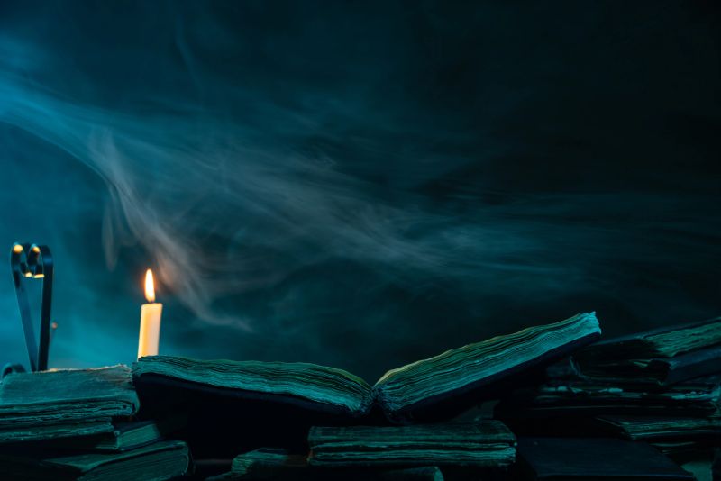 UHD 4K video of open antique book under candlelight in dark. No people are seen in frame. Candle is on the left side of frame. The atmosphere is foggy. Shot with a full frame mirrorless digital camera.