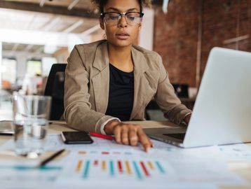 Professional woman analyzing charts and working on laptop in office.