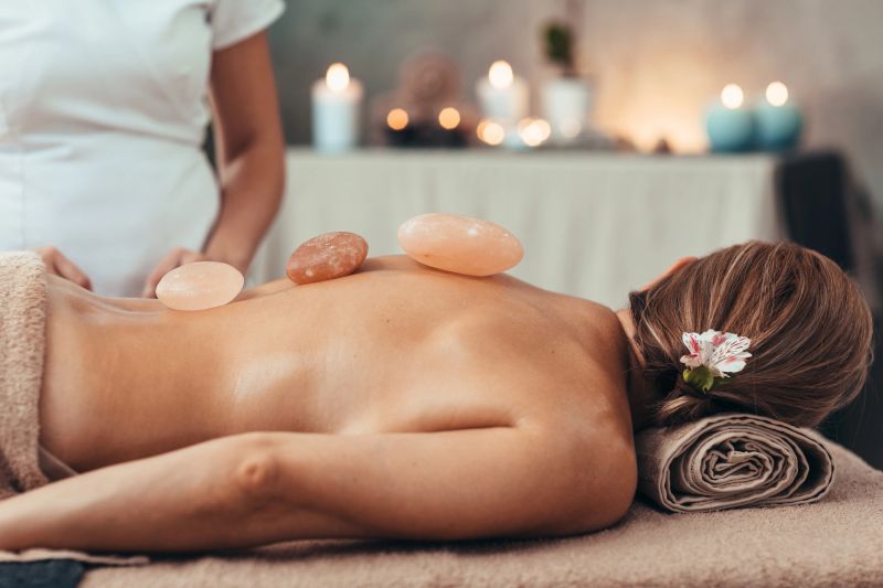 Beautiful woman relaxing during back massage at the spa. Massage therapist applying Himalayan salt stones