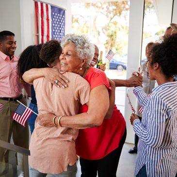 Family members warmly embrace and celebrate with American flags indoors.