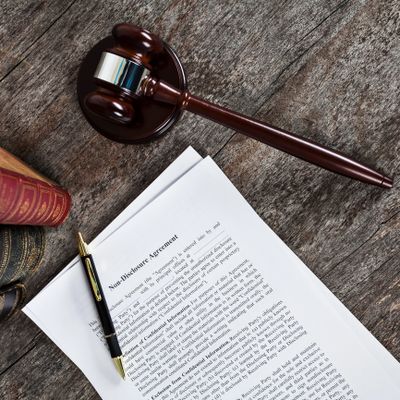 Gavel, pen, and legal documents on wooden surface beside law books.
