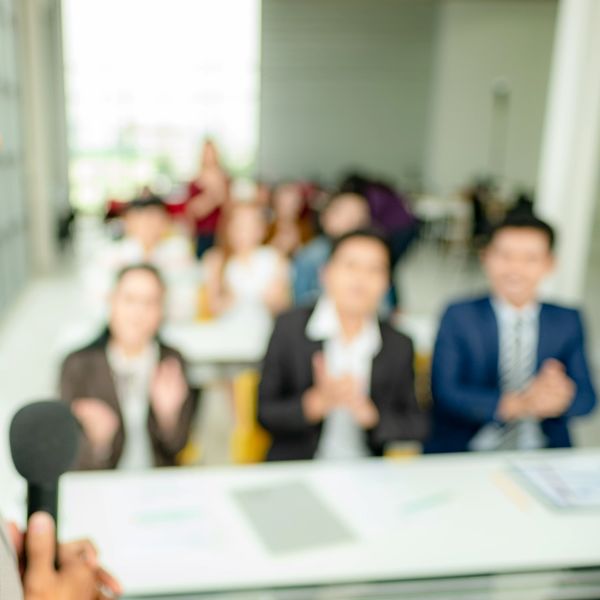 Blurry image of people clapping during a presentation in a bright room.