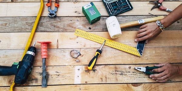 Various hand tools and a person's hands on a wooden surface.