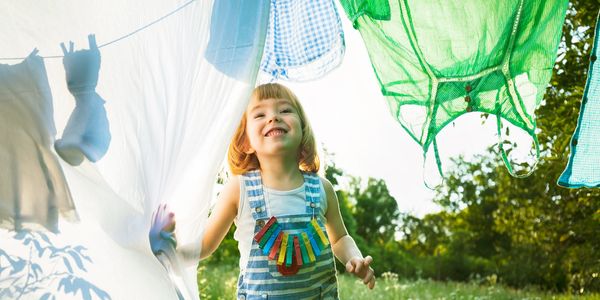 A joyful child playing among hanging laundry outdoors on a sunny day.