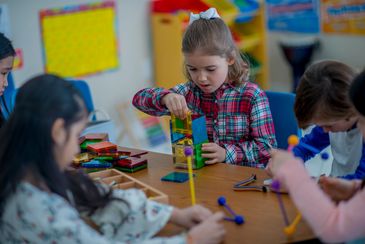 Children building geometric shapes with colorful sticks and connectors in a classroom.