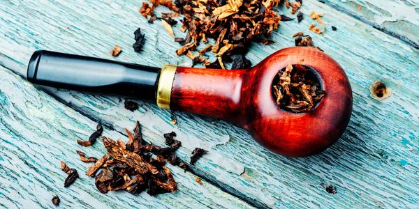 A wooden smoking pipe filled with tobacco on a rustic blue surface.