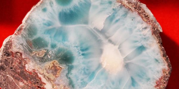 Polished slice of blue-green larimar gemstone on a red background.