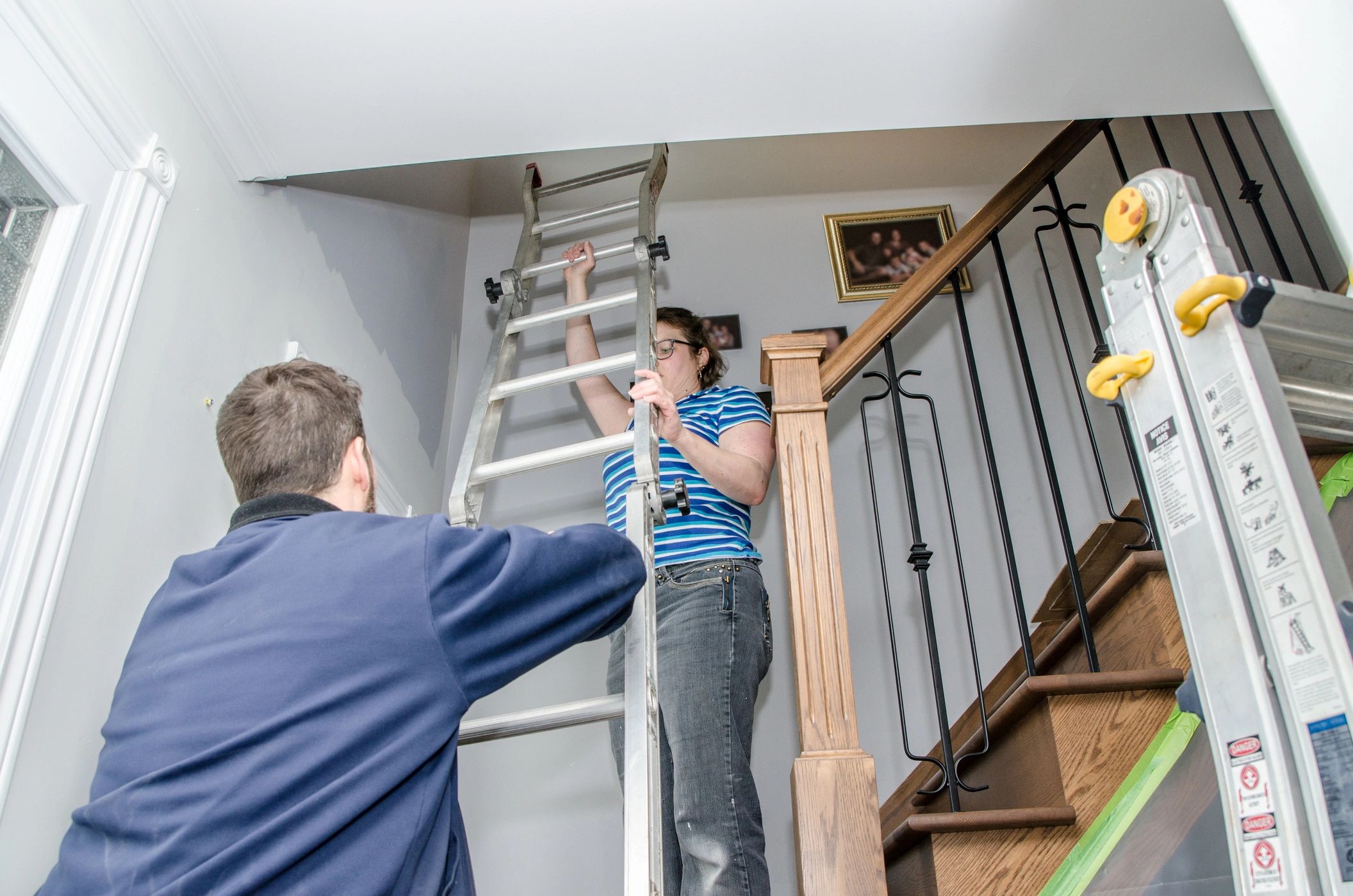Two people handling a ladder near a staircase.