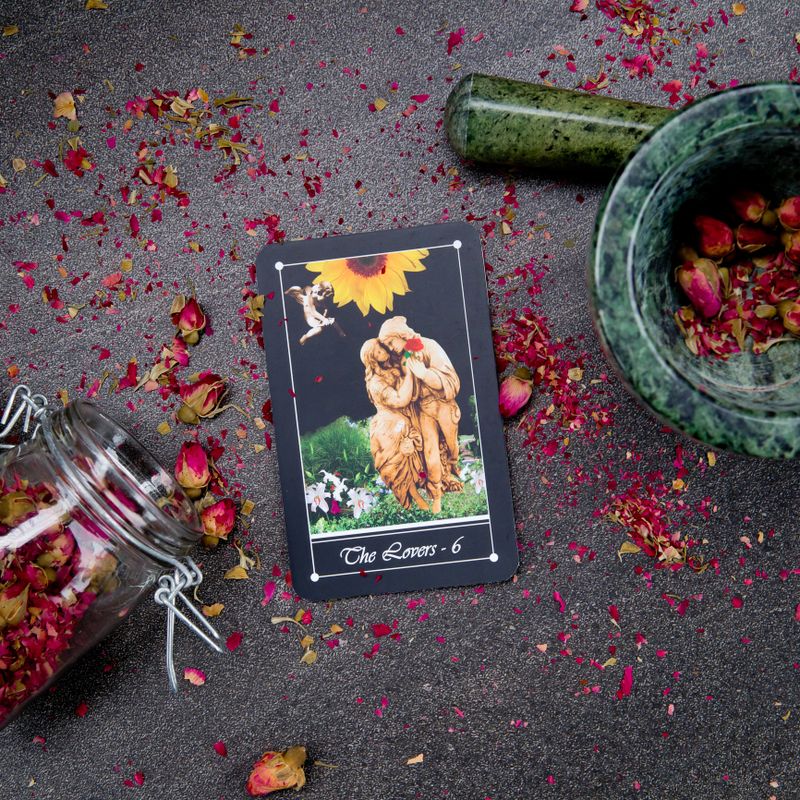 The Lovers card from the Tarot Major Arcana on a card stand with pink dried rose buds and green marble mortar and pestle on gray slate background