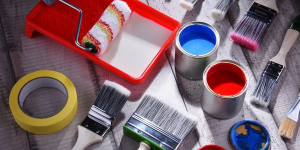 Painting supplies including brushes, paint cans, roller, and tape on wooden surface.