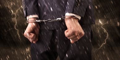 Man in handcuffs wearing a suit, standing in rain with lightning in the background.