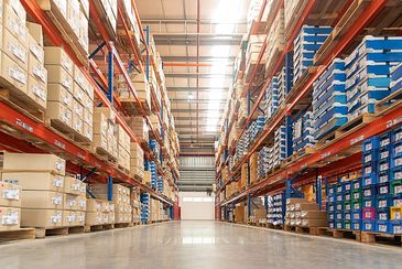 A large warehouse aisle filled with neatly stacked cardboard boxes and blue crates.