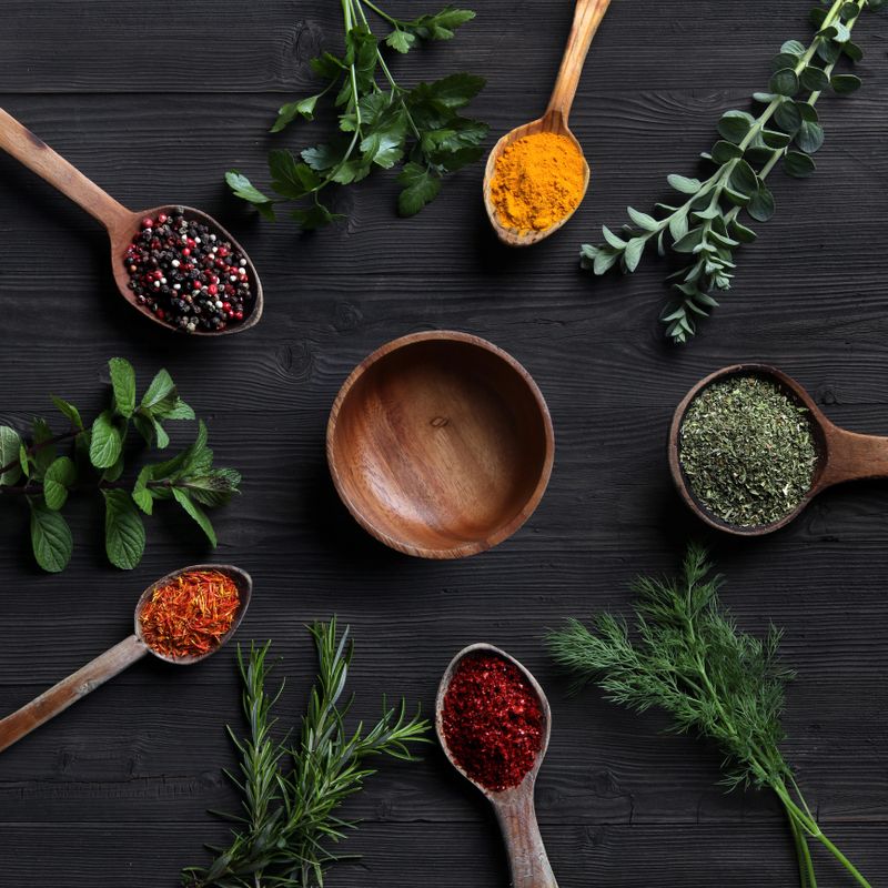 Spices and herbs with old wooden spoons on wooden background