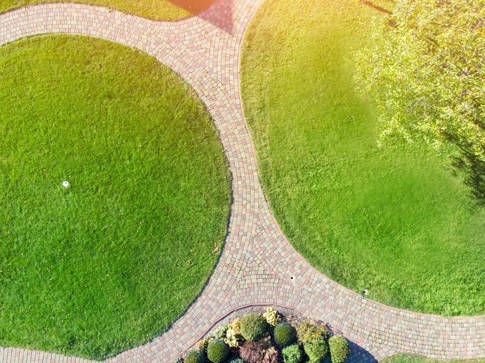 Aerial drone view of backyard garden with circle wath path, green grass lawn and trees. Landscape design and gardening.