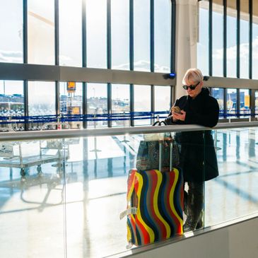 A person using a phone at an airport with colorful luggage.