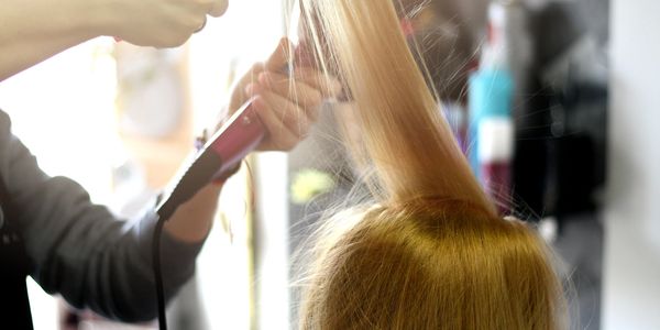 Person blow-drying blonde hair at a salon.